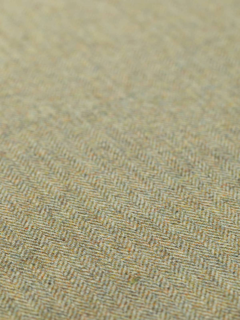 A flat, angled view of Marvellous Moss fabric, displaying the intricate herringbone weave. The golden-green-beige tones, reminiscent of moss on dry stone walls, are vividly captured, with the subtle grey warp yarns adding depth. The medium-weight and textured drape of the fabric are clearly visible.