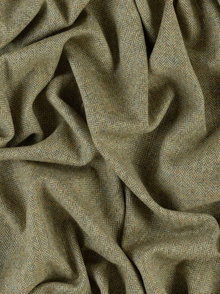 An aerial view of Marvellous Moss fabric, twisted to emphasize the chevron pattern and the blend of golden olive and green hues. The fabric’s natural, earthy tones and the contrast between the weft and warp yarns highlight its rich, moss-like texture. The fabric’s medium weight and traditional tweedy feel are apparent from this angle.