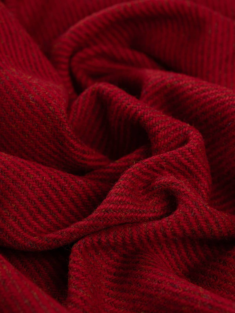 Angled twist shot of Crimson Vale tweed showing its rich crimson, garnet, and berry melange tones with subtle gold and blue fibres and a classic twill texture.
