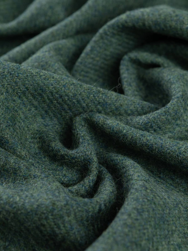 Angled twist shot of Heathfield Yorkshire Tweed showing its loden green, soft teal, and mist-grey melange with a rich, heritage-style twill texture.