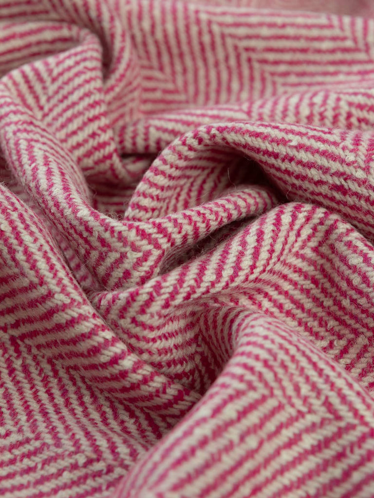 Angled twist shot of the jumbo herringbone lambswool tweed showing its winter-white and fuchsia pink chunky yarns and bold, rustic chevron texture.
