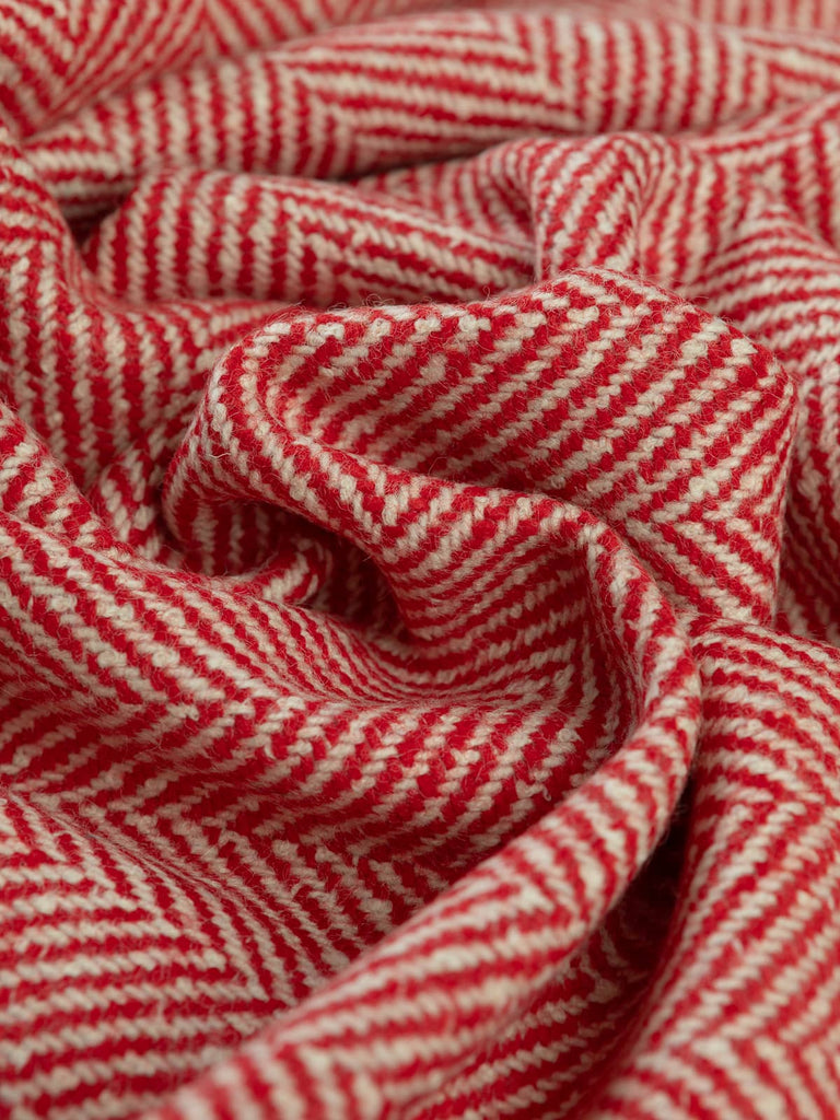Angled twist shot of the jumbo herringbone lambswool showing chunky natural white and holly-berry red yarns forming bold chevrons with a cosy felted texture.
