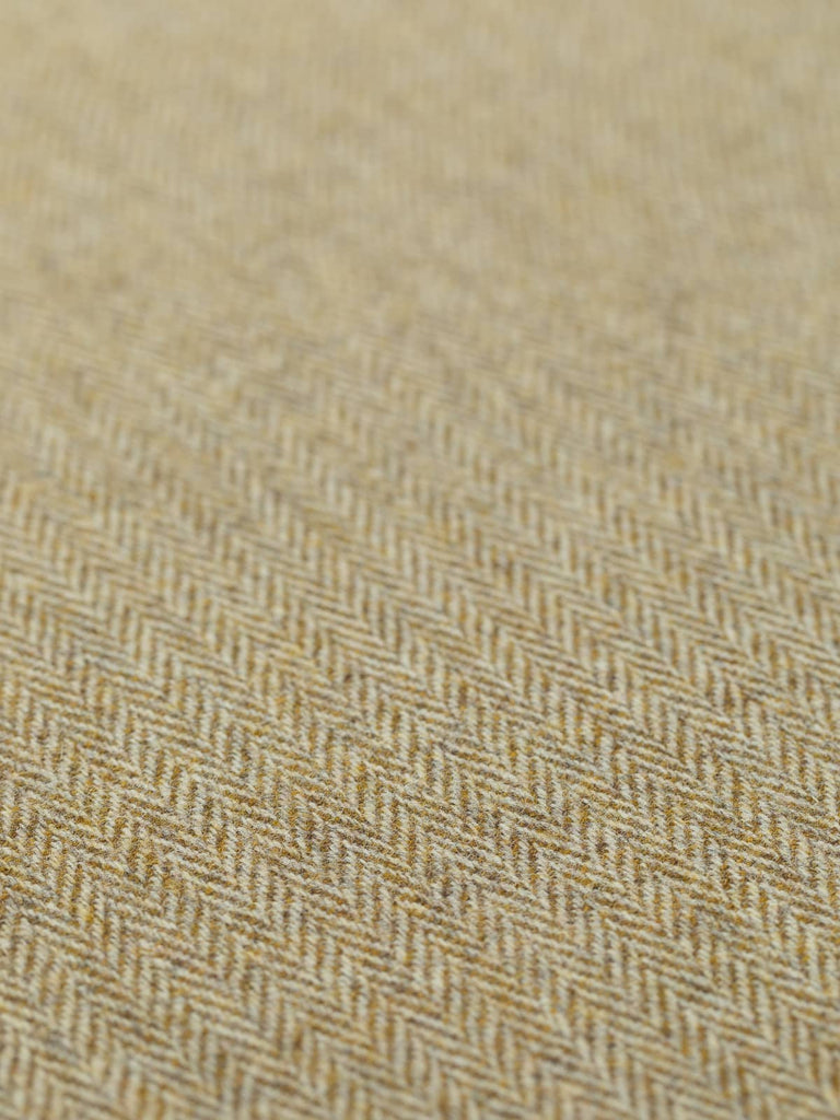 A detailed view of the flat Turning Seasons fabric, showcasing the classic herringbone pattern in soft, sun-infused olive green hues. The alternating golden olive and natural white threads create a gentle, textured effect, reflecting the fabric’s mellow, nature-inspired palette. This close-up captures the medium-weight, traditional tweed feel, perfect for stylish, timeless creations.