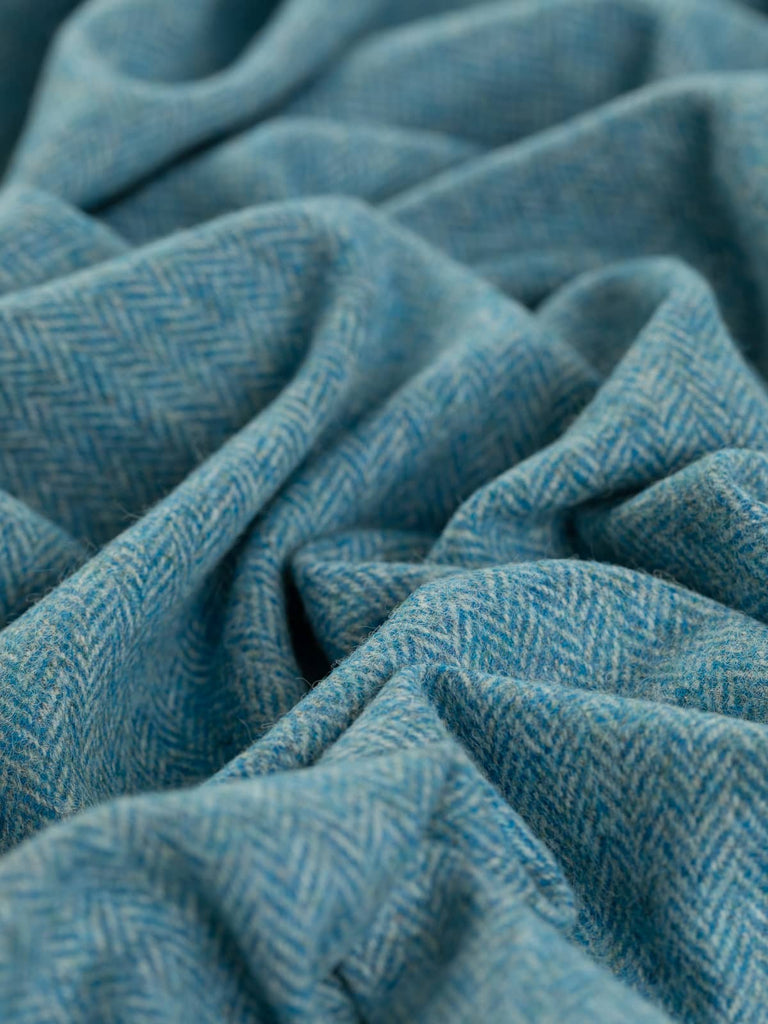 A close-up shot of the Yorkshire Tweed Herringbone - Waterside 2, twisted to showcase the fine chevron pattern. The frosty grey-green warp contrasts beautifully with bright turquoise weft yarns, evoking the striking colors of a kingfisher in flight. The intricate herringbone weave is highlighted, emphasizing the fabric’s texture and the cool, refreshing palette.