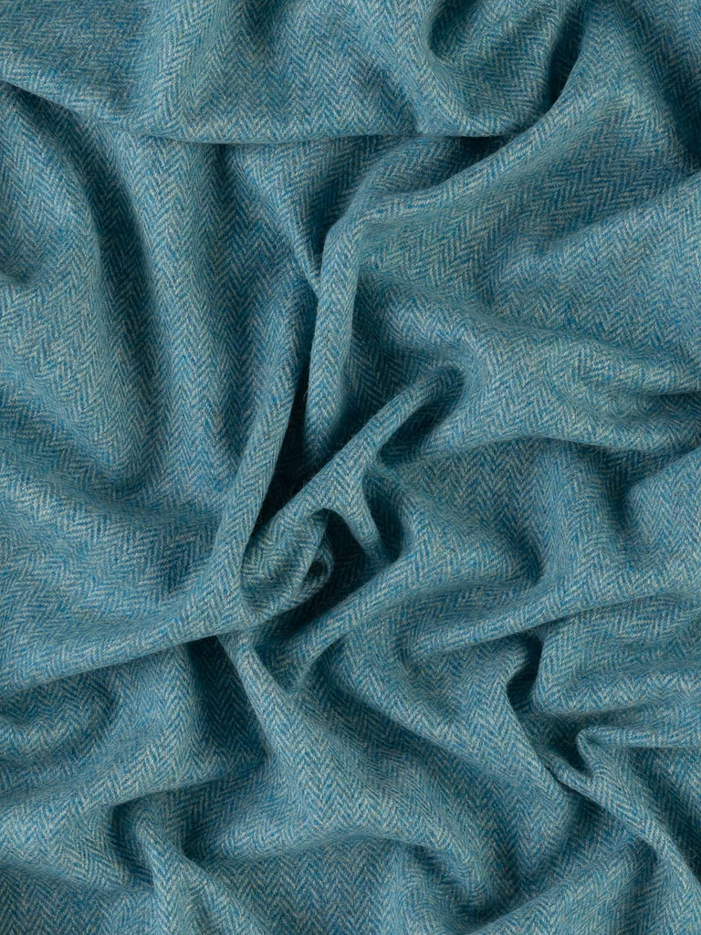 An aerial view of the Waterside 2 herringbone tweed, artistically twisted to display the vibrant turquoise and frosty grey-green tones. The image captures the delicate chevron design and luxurious wool texture, evoking the cool, flowing hues of a tranquil stream. This versatile fabric brings a fresh, nature-inspired aesthetic to both fashion and interiors.