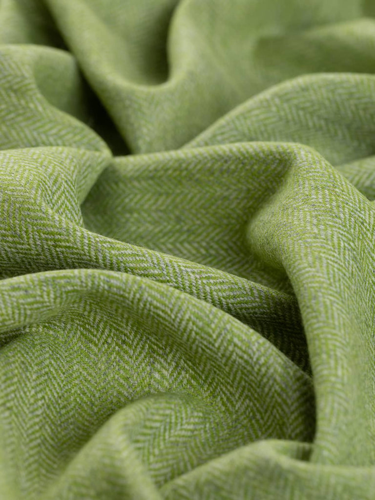 A close-up of the Yorkshire Tweed Herringbone - Spring Fling fabric, twisted to showcase its lively chevron pattern. The vibrant lime green weft is balanced by soft marl grey warp yarns, creating a fresh and dynamic texture that captures the essence of new spring growth. The herringbone weave is intricately highlighted, evoking the fern-like details of the pattern.