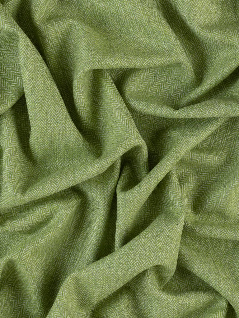 An aerial view of the Spring Fling herringbone tweed, artfully twisted to showcase the interplay of vibrant lime green and tempered marl grey yarns. The image highlights the delicate chevron design, reflecting the lively energy of springtime. The luxurious wool fabric promises versatility and warmth, ideal for both fashion and interior projects.