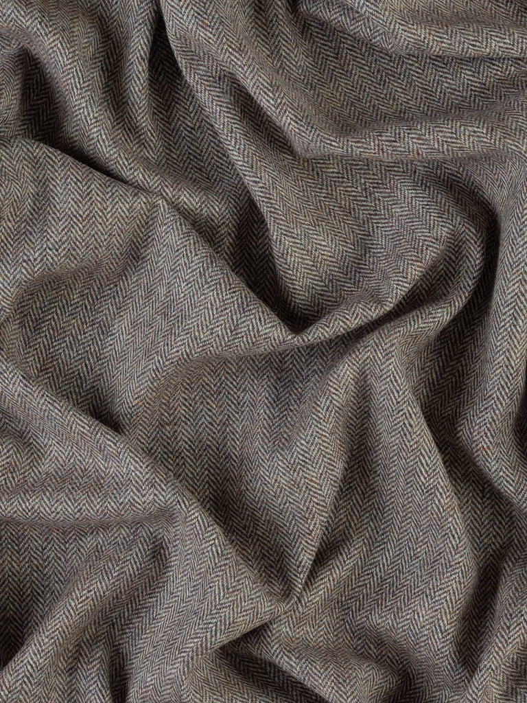 An aerial view of the Heather Momento fabric, artfully twisted to highlight its complex color palette of heather purple, rust, and gold. The soft chevrons of the herringbone weave are prominently visible, reflecting the fabric’s medium weight and rich texture. The image captures the fabric’s comforting drape and warm feel, perfect for both fashion and interior applications.