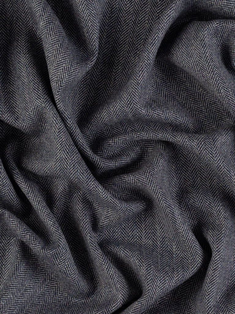 A twisted aerial view of the Eco Herringbone Yorkshire Tweed - Blackthorn Blue, highlighting the distinctive herringbone weave with alternating lilac, beige, and grey hues against dark navy weft threads. The fabric’s medium-weight drape is demonstrated as it twists gently, emphasizing the luxurious feel and soft texture that embody the essence of traditional English craftsmanship.