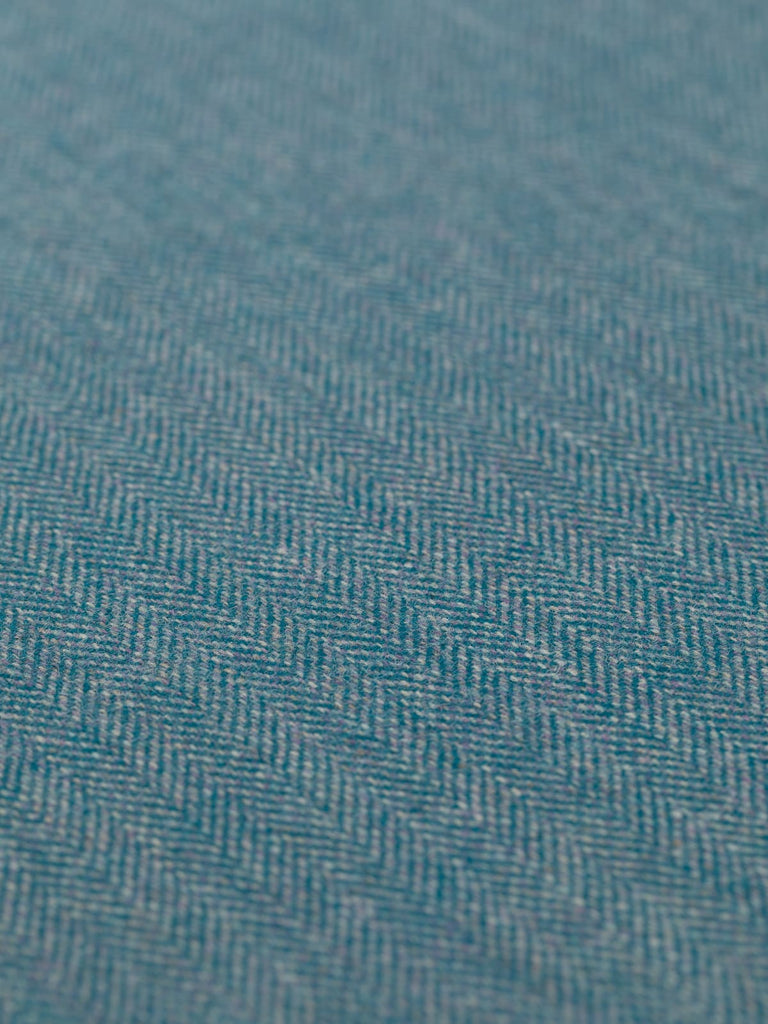 Angled detailed close-up of the Eco Herringbone Yorkshire Tweed in Teal Tale, displaying the flat weave and subtle sheen. The interplay of teal and lilac tones with the characteristic chevrons of the herringbone pattern is highlighted.