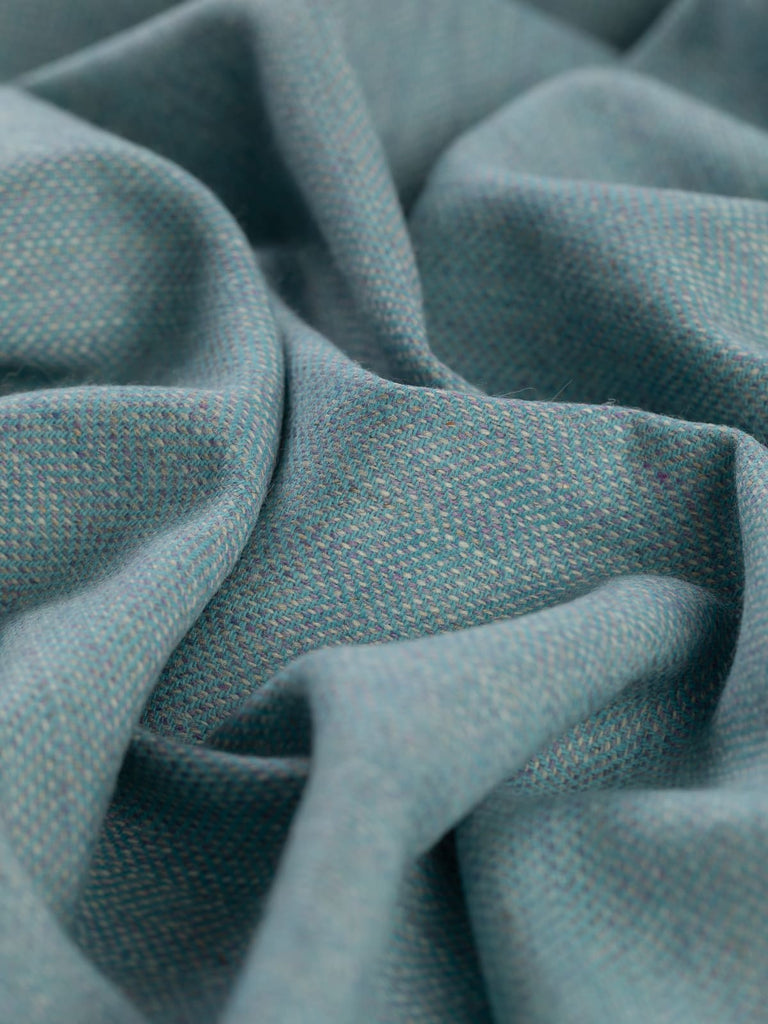 Angled close-up of the twisted Eco Herringbone Yorkshire Tweed in Frosted Valley, highlighting the intricate herringbone design. The fabric features a cool aqua and lilac color scheme with a textured appearance.