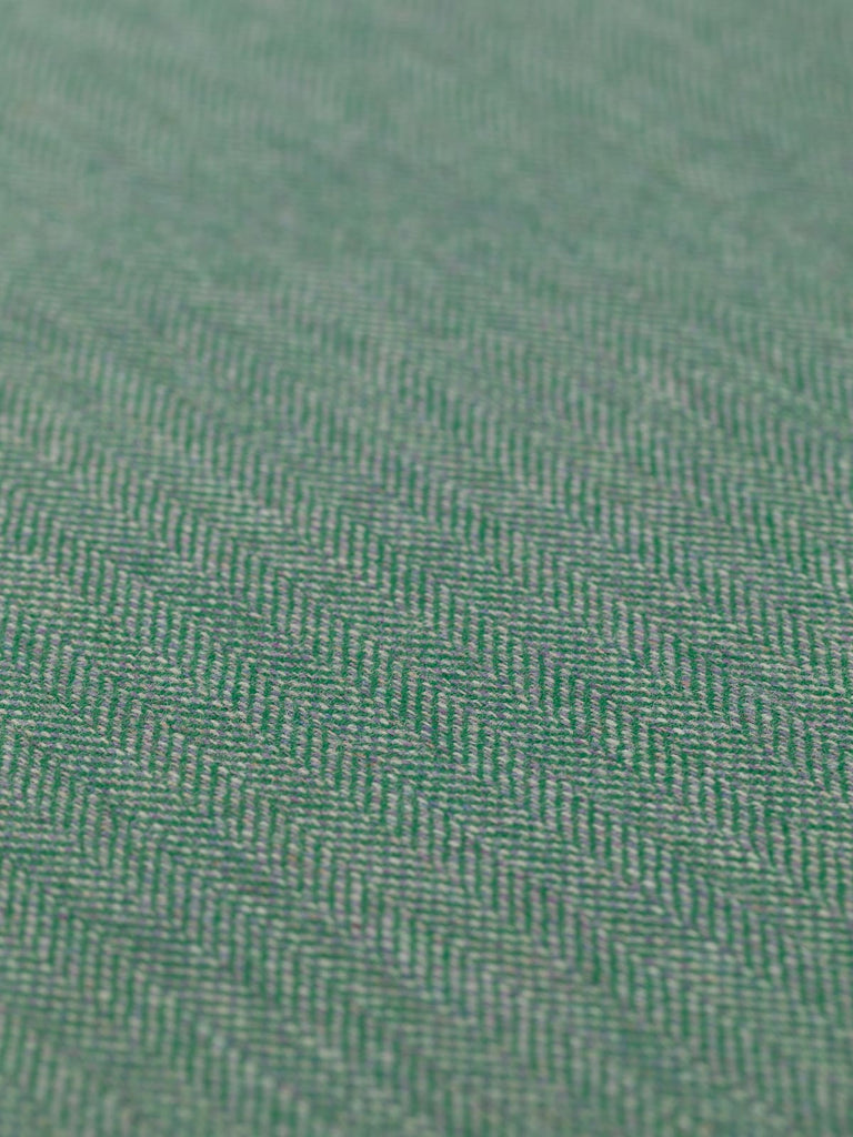 Angled detailed close-up of Eco Herringbone Yorkshire Tweed in Verdant Valley, highlighting the flat weave and rich emerald green with lilac undertones. The unique herringbone pattern and the fabric’s vibrant, textured appearance are prominent.