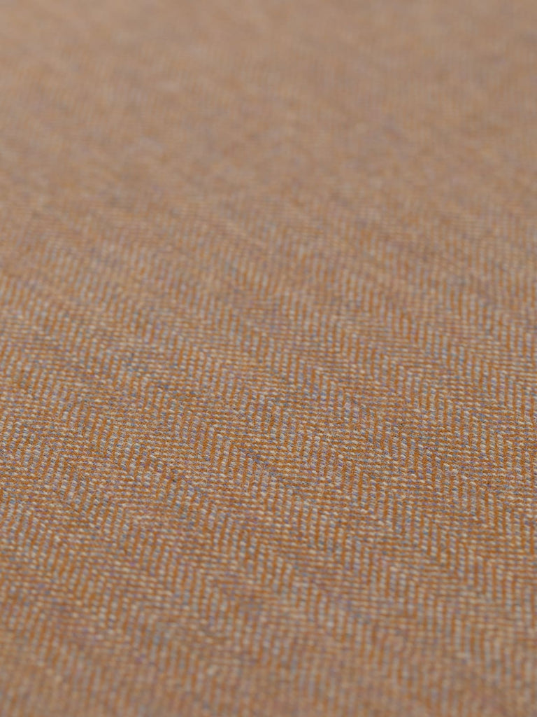 Angled detailed close-up of Eco Herringbone Yorkshire Tweed in Barley Bounty, focusing on the flat weave and warm golden ochre with lilac undertones. The distinctive herringbone pattern and the fabric’s nuanced texture are clearly visible.