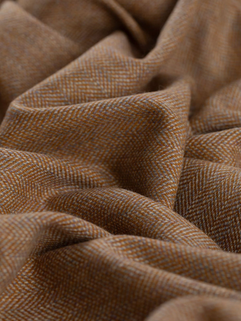 Angled close-up of the twisted Eco Herringbone Yorkshire Tweed in Barley Bounty, emphasizing the rich golden ochre and subtle lilac highlights. The intricate herringbone pattern and the fabric’s soft texture are prominently featured.