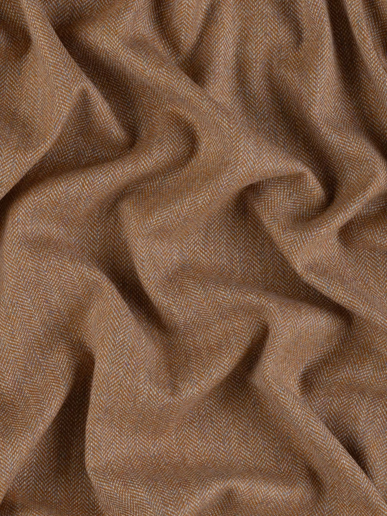 Aerial view of Eco Herringbone Yorkshire Tweed in Barley Bounty, twisted to display the full width and pattern. The fabric’s golden ochre and misty lilac hues, combined with its characteristic herringbone weave, create a rich and inviting visual.