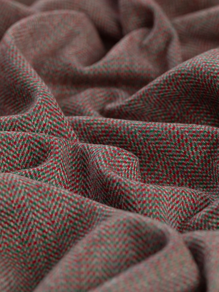 Angled close-up of twisted Eco Herringbone Yorkshire Tweed in Festive Folly, showcasing the festive red and green hues. The herringbone pattern and soft texture are prominent, emphasizing the fabric's holiday-inspired design.