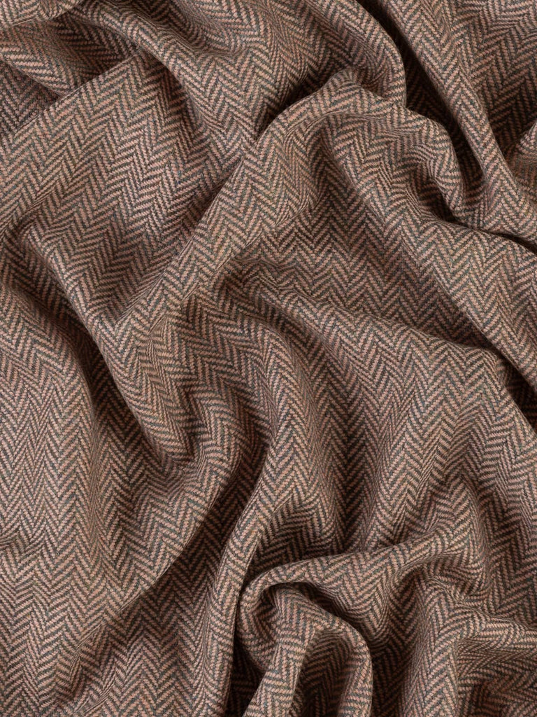 An aerial view of the Nostalgic Blush fabric, artfully twisted to emphasize the large herringbone chevrons. The combination of grey, green, and subtle brown tones set against the gentle blush pink weft creates a unique and sophisticated look. The fabric's soft, brushed texture and supple drape are captured, reflecting the high-quality craftsmanship and nostalgic allure.