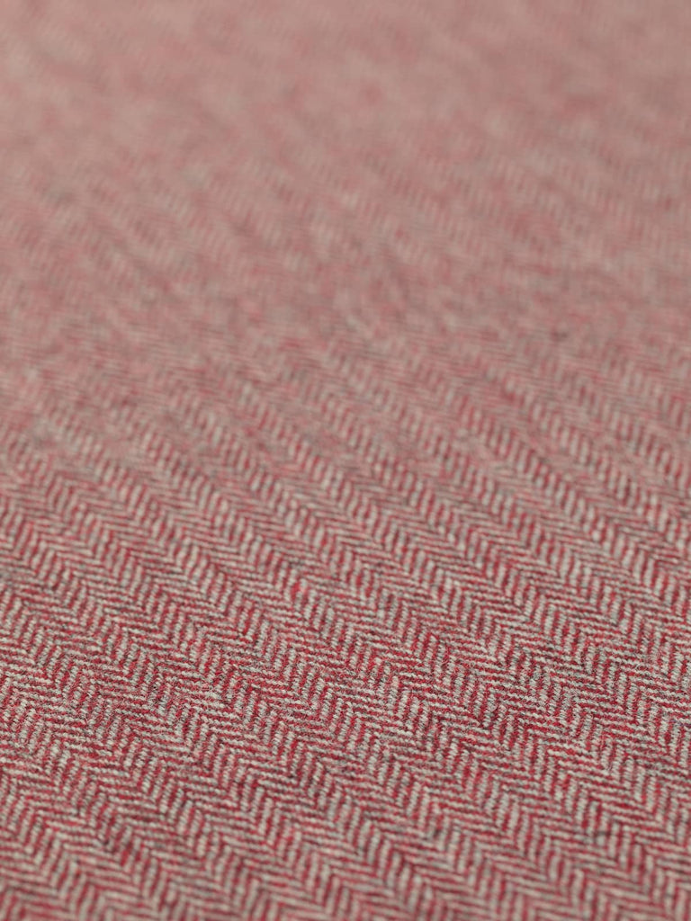 A detailed flat image of Lifeblood, showing the fine herringbone pattern with multitoned hues of rich red. The subtle grey warp yarns provide a complementary base, enhancing the overall appearance of glossy, berry-like reds. The fabric’s medium-weight, soft texture, and stable handle are clearly visible, emphasizing its versatility and timeless appeal.