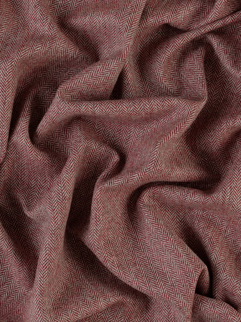 An aerial view of the Lifeblood fabric, twisted to emphasize the chevron pattern and rich color palette. The deep red hues are reminiscent of winter berries, highlighted against the natural grey tones, creating a bold yet classic look. The close weaving and soft texture showcase the fabric’s quality and promise of cosy warmth, perfect for A/W wardrobe staples and home furnishings.