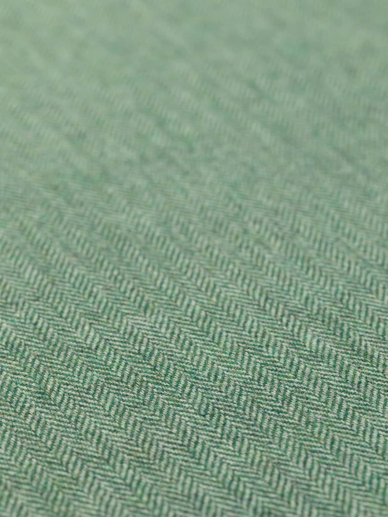 A detailed flat view of Green Pastures fabric, highlighting the fine herringbone weave and rich green hue. The blend of glaucous green and grey yarns creates a fresh, grass-like appearance, reminiscent of early summer pastures. The close weave and medium-weight drape are clearly visible, emphasizing the fabric’s cosy warmth and timeless tweedy feel.