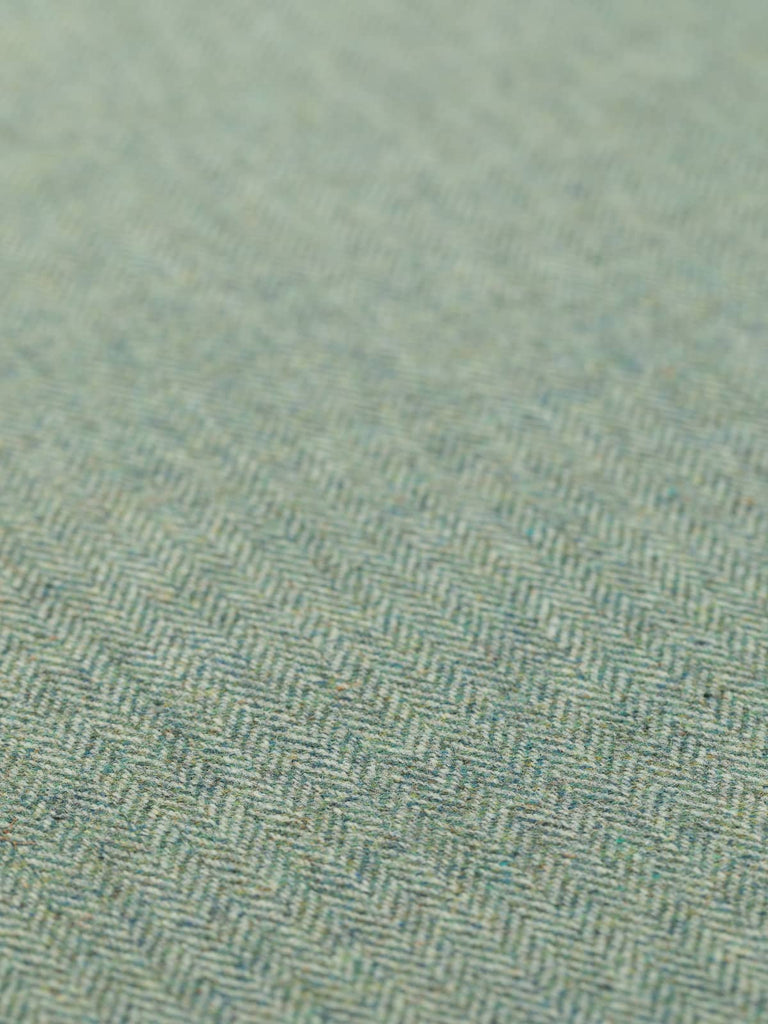 A flat, angled view of Moonlit Lichen fabric, emphasizing the delicate grey-green tones and the characteristic herringbone weave. The blend of blue-green and grey yarns creates a sophisticated, moonlit effect, with the traditional tweed texture and medium weight evident in the fabric’s drape.