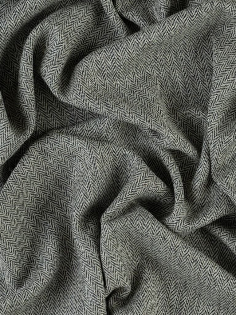 An aerial view of Tempest fabric, twisted to reveal the chevron pattern and the dynamic contrast between the storm grey and deep navy blue. The fabric’s medium weight and the fine herringbone detail are highlighted, giving a sense of the sophisticated, tempestuous effect of the yarns.