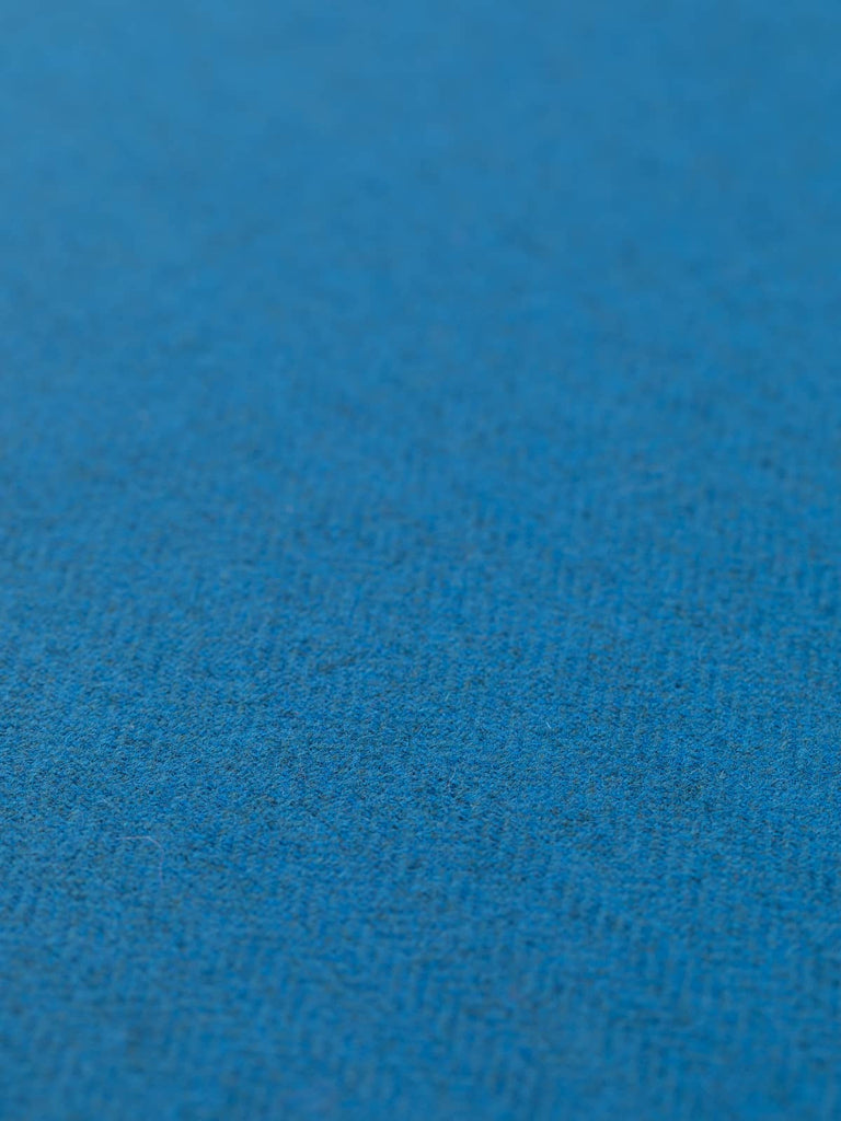 Angled flat view of Autumn Azure lightweight lambswool herringbone fabric, 290gsm, displaying rich azure blue hue inspired by Yorkshire skies and Michaelmas daisies, woven through soft grey melange yarns