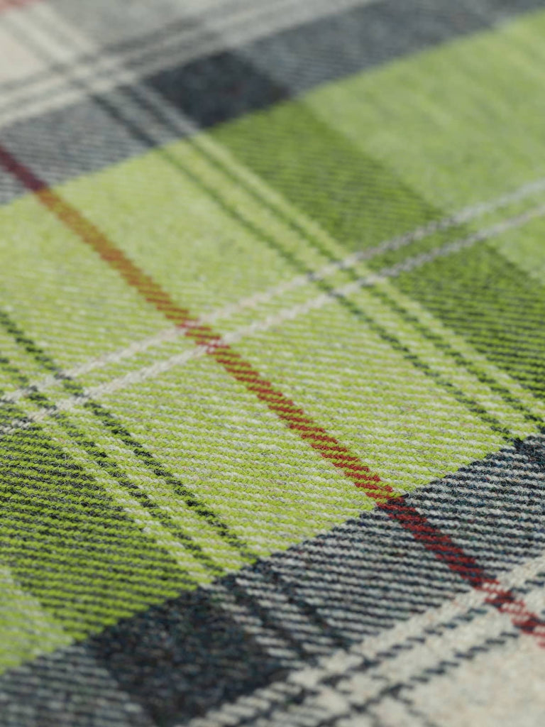 Angled flat view of Green Awakening Heritage Plaid, medium-weight wool tweed with 25cm x 27cm repeat, highlighting spring-inspired palette of fresh greens, rain-soaked greys, and bright red accent stripe