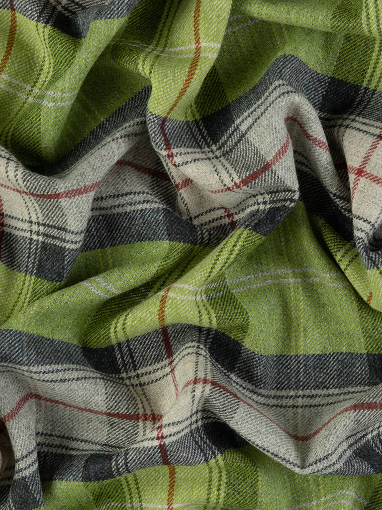 Overhead flat shot of Green Awakening Yorkshire woollen plaid, capturing natural early-spring colour blend of green shoots, misty grey, charcoal stone, and red check detail across fibrous wool texture