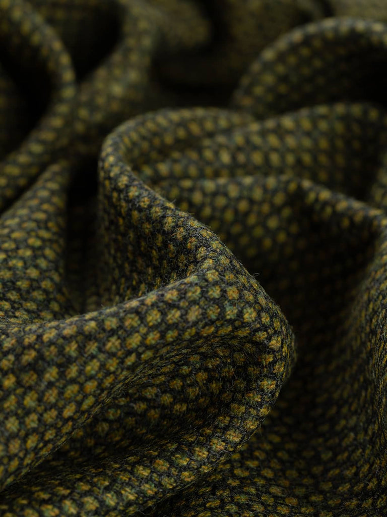 Twist of Greenewt Yorkshire Wool Birdseye Tweed, 100% wool, 280gsm, showing its intricate melange of moss, algae, and golden green tones with subtle charcoal speckling and soft woollen texture.