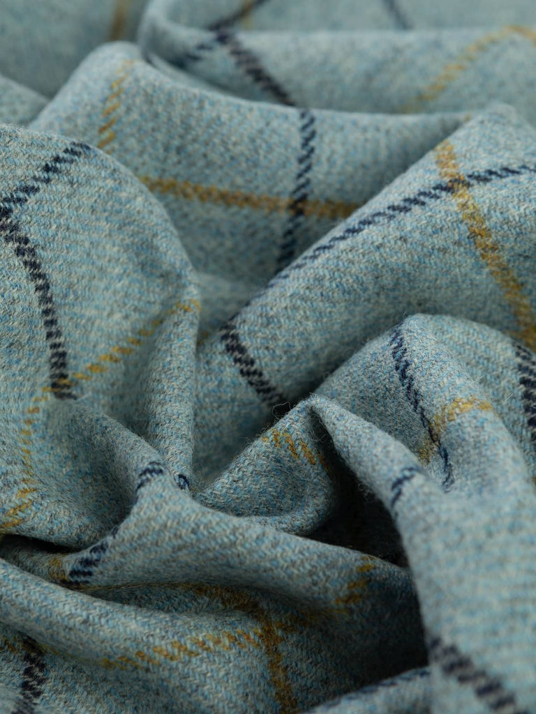 Angled twist shot of Harborton Yorkshire Tweed, showing the steel-grey and sea-washed blue melange with golden-green and navy windowpane checks twisting across the folds.