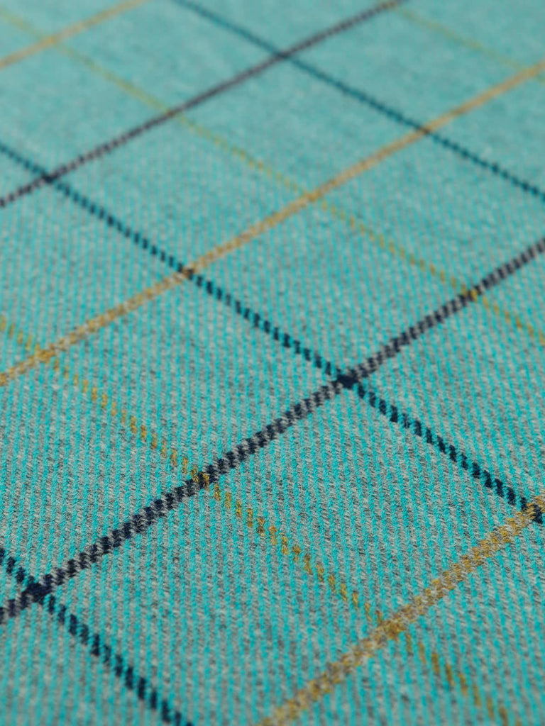 Angles flat shot of Highland Tide tweed, revealing its turquoise and grey melange base, crisp navy overchecks, and golden windowpane lines with subtle greenish tones.