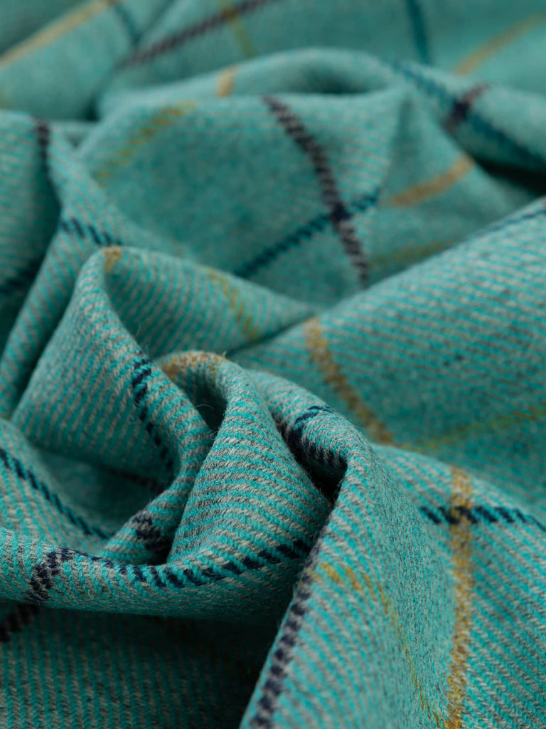 Aerial twist shot of Highland Tide fabric, capturing twisted folds from above and highlighting the interplay of grey marl, vivid turquoise, navy shading and glinting gold checks.
