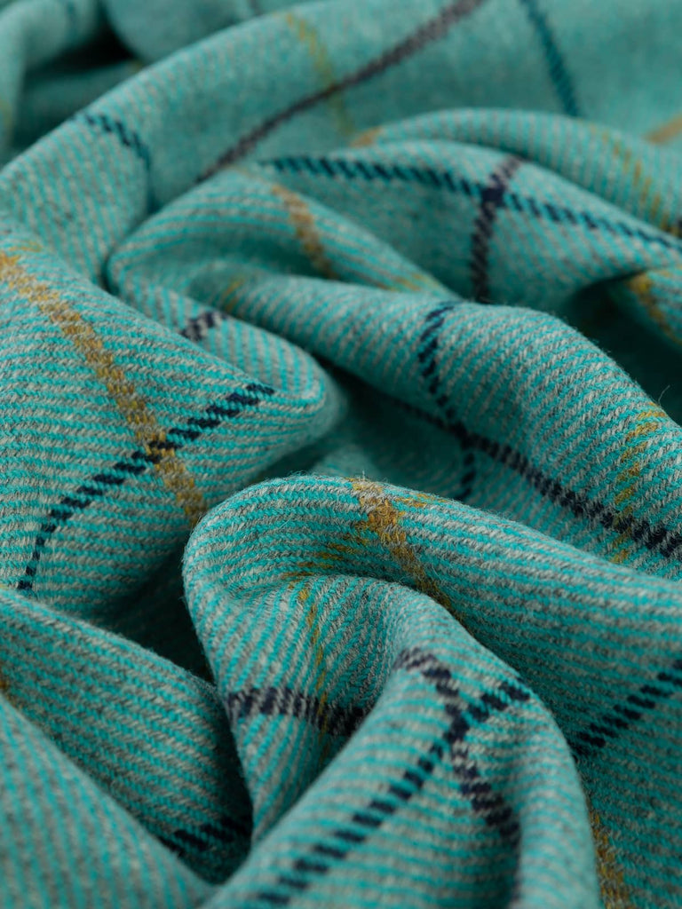 Angled twist shot of Highland Tide Yorkshire Tweed, showing mist-grey marl warp with kingfisher turquoise weft and navy and sunshine-gold windowpane checks.