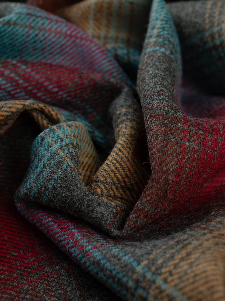 Angled twist shot of Jewel Glen Check Yorkshire Tweed, showing heathland grey-green and bracken brown base with glowing amber, ruby and aquamarine twill overchecks.