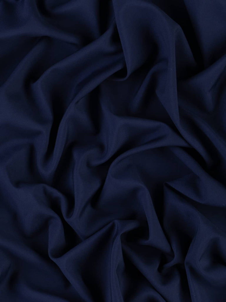 Indigo Dream fabric in 100% Wool, folded to showcase its rich indigo and French navy hue. The fabric has a semi-matte finish and fine twill weave, exuding a luxurious appearance. Light to medium-weight, it features a stable hand lengthwise with natural width-wise ease, perfect for sophisticated garments.