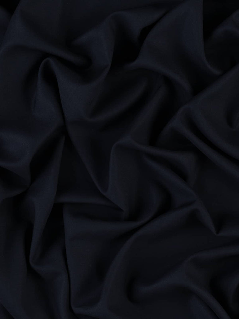 Twisted aerial view of Navy Zenith, a 100% Virgin Wool Tropical Suiting fabric in a deep, rich navy tone. The fabric showcases a lightly textured surface and a breathable, fluid drape. The lightweight wool is perfect for warm climates, offering excellent crease resistance and a smart, versatile style ideal for suiting and elegant separates.