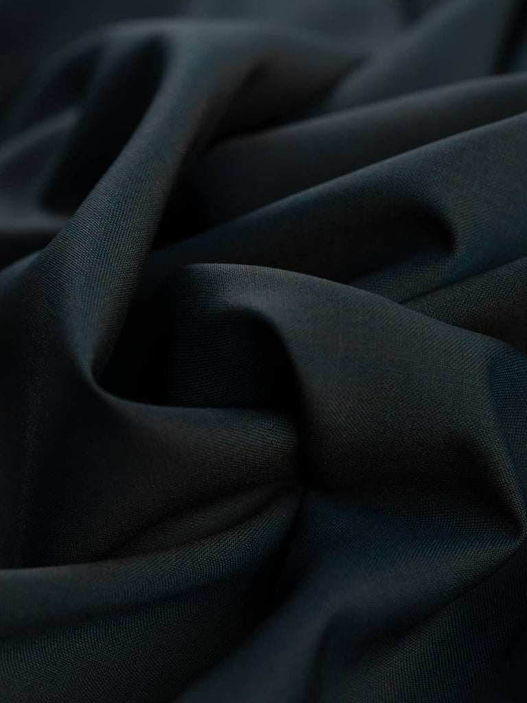 Ocean Mystery wool fabric spread out, showcasing its sleek, matte weave and subtle blue-green tones with mysterious undertones. Ideal for creating elegant, crease-resistant garments like skirts, jackets, and suits.