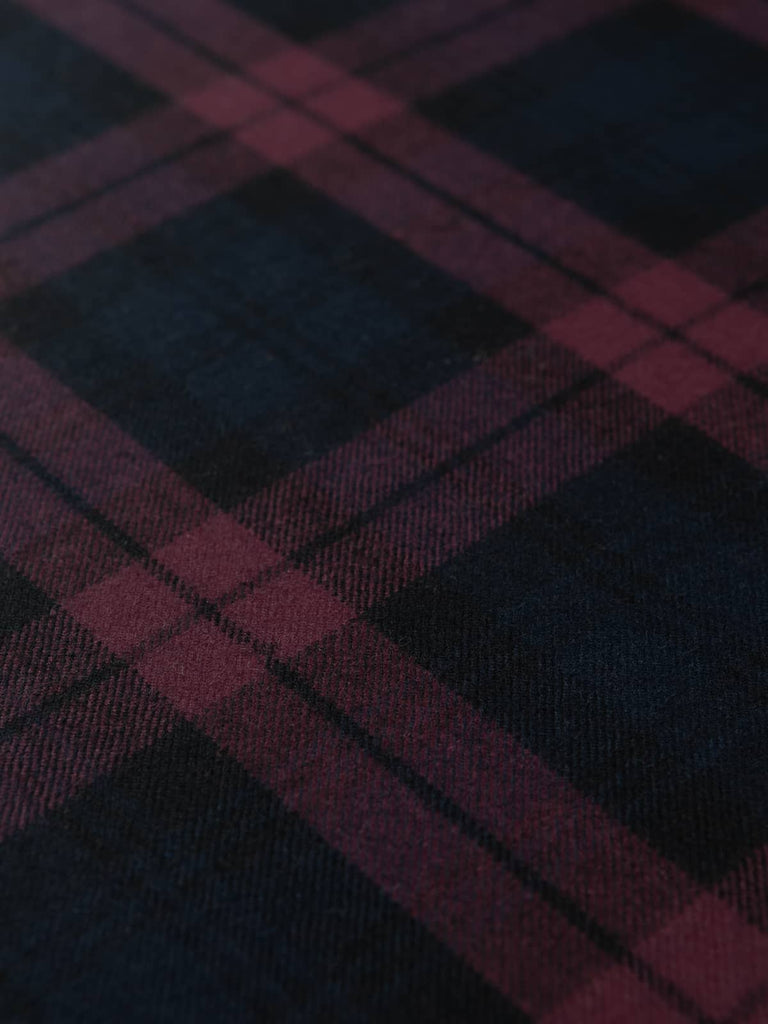 Flat lay of Plum Watch Tartan fabric displaying rich plum, navy, and black tartan sett in soft brushed lambswool, woven in Yorkshire with fine detail.
