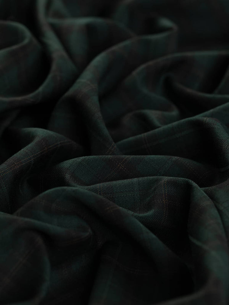 Close-up of the Bosco di Notte Check fabric, showing its smooth superfine twill weave and subtle check design. The combination of black, spruce green, and hazel brown yarns produces a stylish, hardwearing fabric with an elegant drape, ideal for jackets, skirts, and tailored suits.