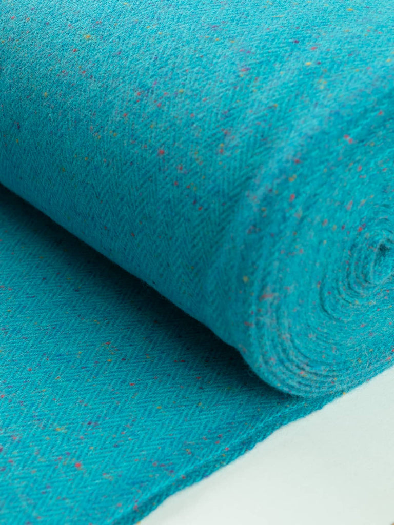 In this angled view of the Electric Turquoise fabric laid flat, the striking chevrons emerge prominently, highlighting the vivid turquoise yarns and deeper multi-hued tones that create a stunning visual contrast, enhanced by playful flecks of color.