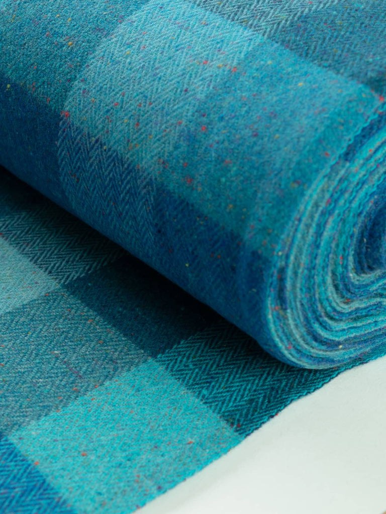 An angled view of the Treasured Oceans fabric laid flat showcases its striking block check pattern, where deep and light blue-green tones interplay beautifully, reminiscent of the diverse colors found in ocean depths.