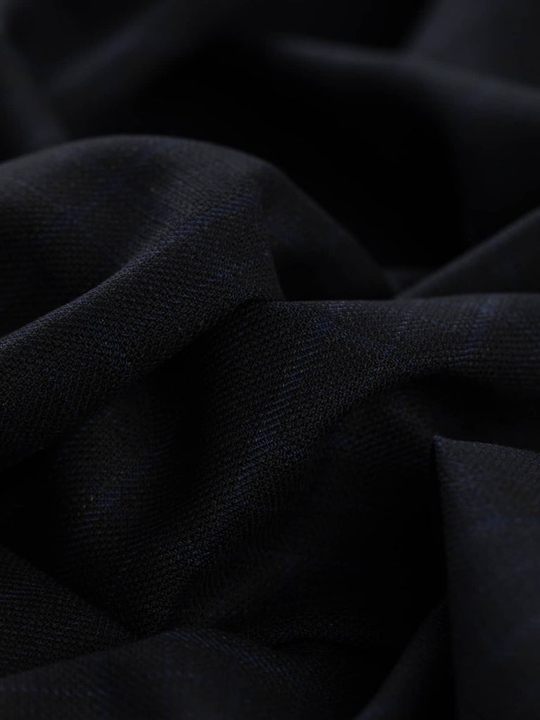 Augustus Check fabric spread out, displaying its subtle yet authoritative windowpane check pattern in almost black and blue hues. The fabric’s breathable, lightly textured weave makes it ideal for warm weather suiting, jackets, and skirts.