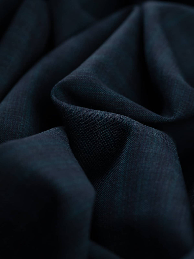  Cosmopolitan Check fabric spread out, revealing its refined, striated check pattern with dark indigo and blue-green tones. The lightweight, crease-resistant weave offers a sleek and drapey finish, perfect for elegant suiting and tailored pieces.