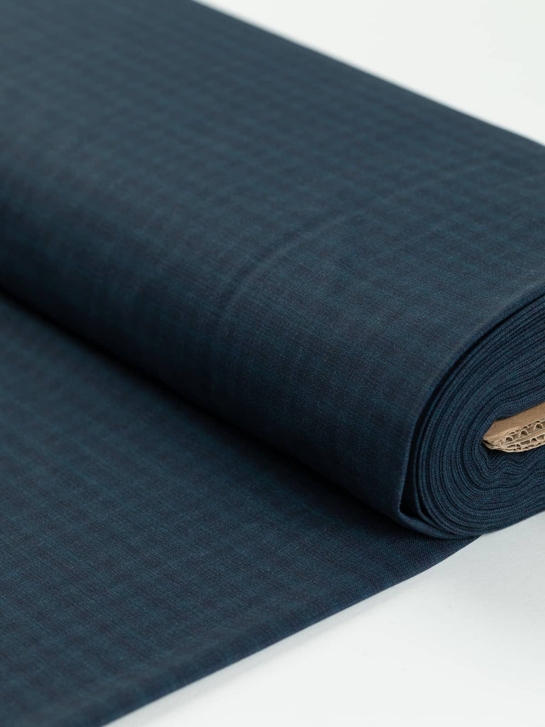 Italian Fine Virgin Wool Worsted fabric, folded to display its sophisticated Cosmopolitan Check pattern in rich dark indigo and Prussian blue hues. The lightweight, flat matte weave showcases a subtle and superfine check, ideal for classic tailored garments.