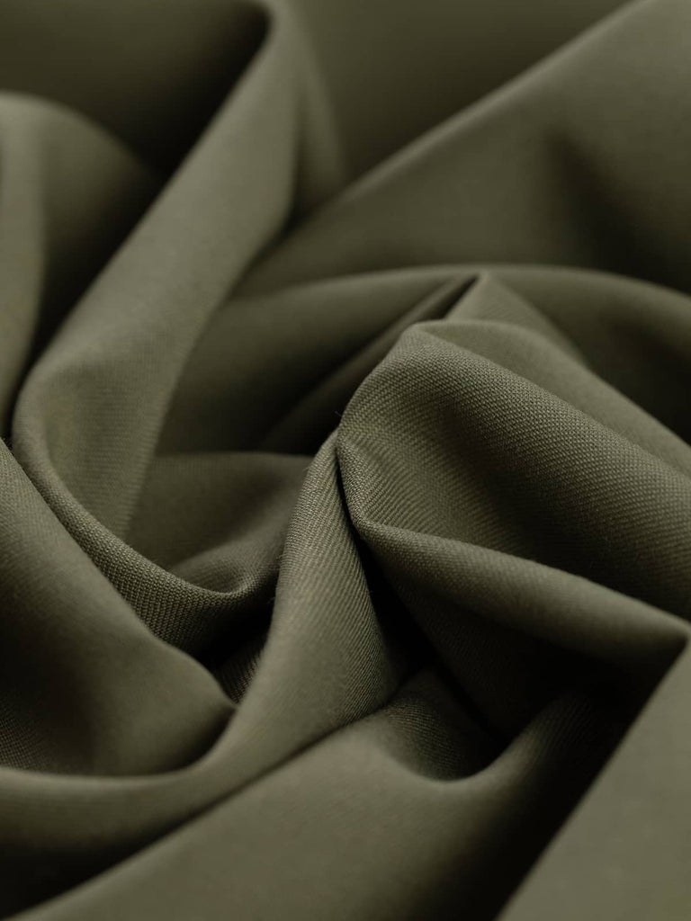 Twisted, angled shot of Dusted Olive fabric, capturing the soft folds and fluid drape of the fine twill weave. The subdued green-beige tone, paired with its smooth texture, conveys a smart, military-inspired aesthetic with a refined finish