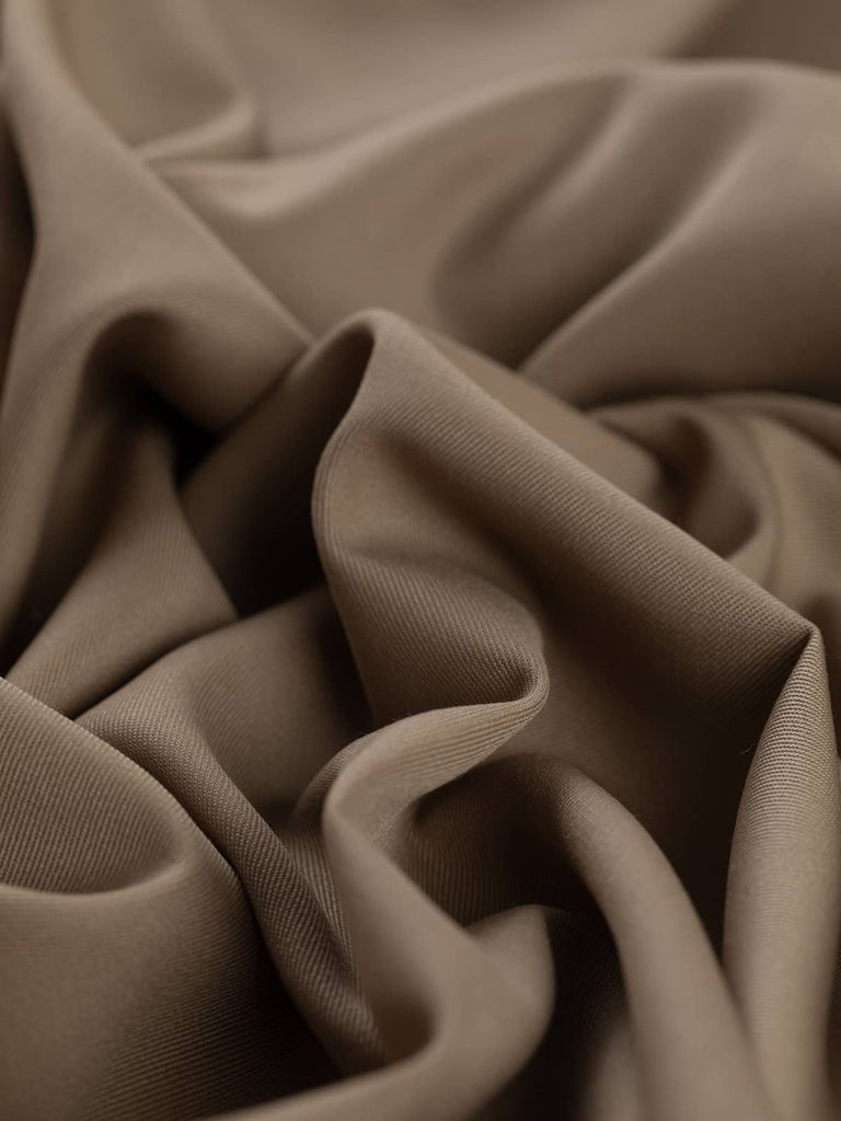 Angled twist shot of the Desert Sand wool-blend fabric, highlighting its fluid drape and tightly woven twill texture. The warm, neutral beige hue catches the light softly, evoking a clean, smart aesthetic with versatile styling potential.