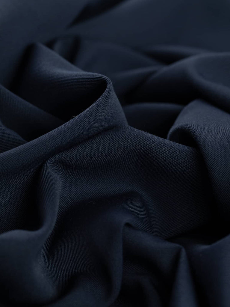 Angled twist shot of Old Navy wool-blend fabric, revealing gentle folds that showcase its soft drape and close twill weave. The deep navy color with grey hints gives the fabric a refined, understated elegance suitable for tailored pieces.