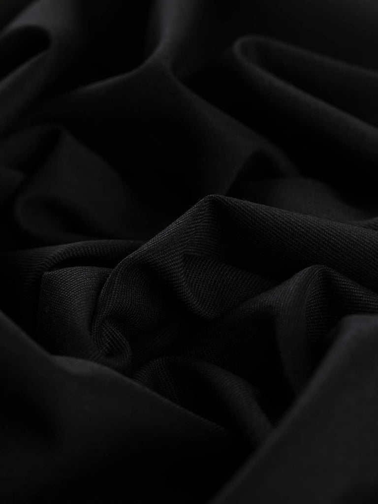 Angled twist shot of Classic Black fabric, showing elegant folds and a soft drape that accentuates its rich black tone and close gabardine weave. The light-catching sheen reflects its polished finish, suitable for everything from formalwear to durable everyday tailoring