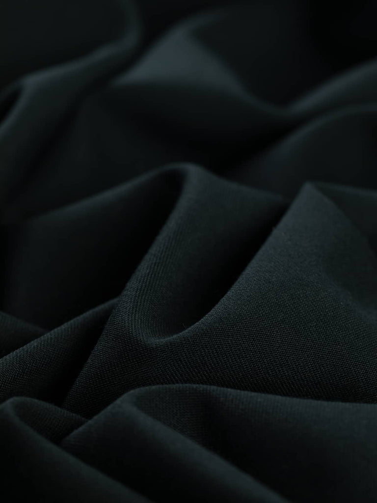 Flat, angled view of Dark Forest fabric, emphasizing its rich dark green hue with a luxurious fine twill weave. The fabric’s substantial drape and versatility make it a fantastic choice for both statement pieces and timeless staples